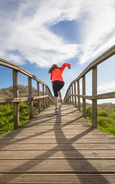 Foto vista traseira de uma garota correndo em um calçadão de madeira