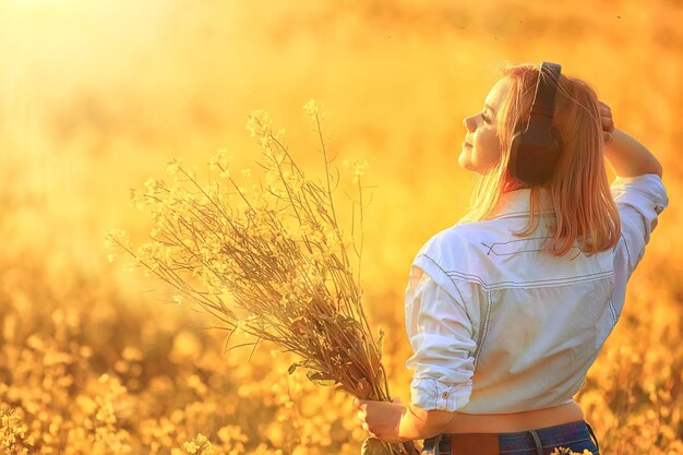 vista traseira de uma garota em fones de ouvido ouvindo música em um campo de flores, a música da primavera está feliz