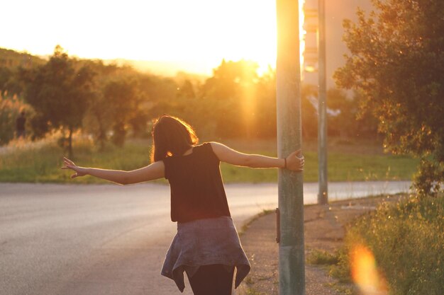 Foto vista traseira de uma jovem brincalhona segurando um poste na estrada