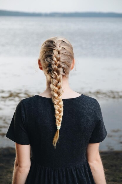 Foto vista traseira de uma jovem com o cabelo trançado de pé na praia