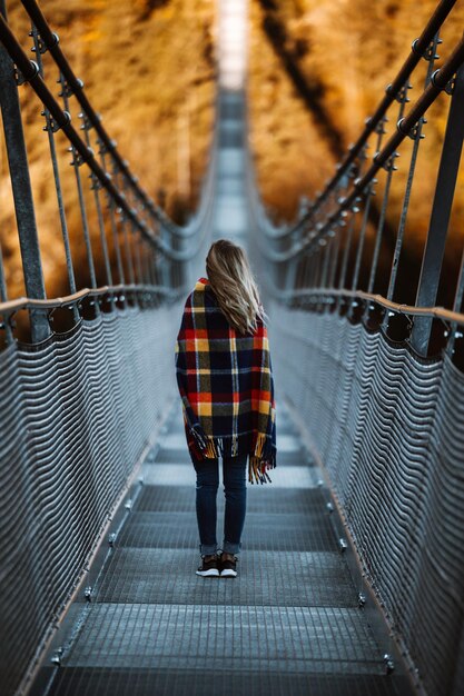 Foto vista traseira de uma jovem de pé em uma ponte pedonal na floresta durante o outono