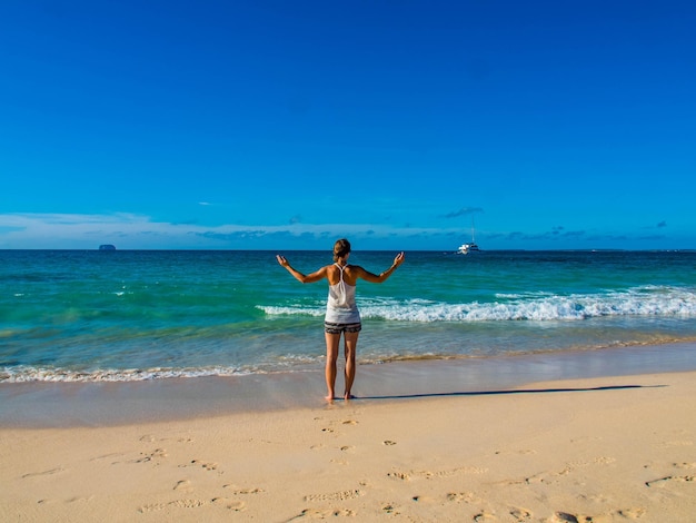 Foto vista traseira de uma jovem de pé na praia contra um céu azul claro