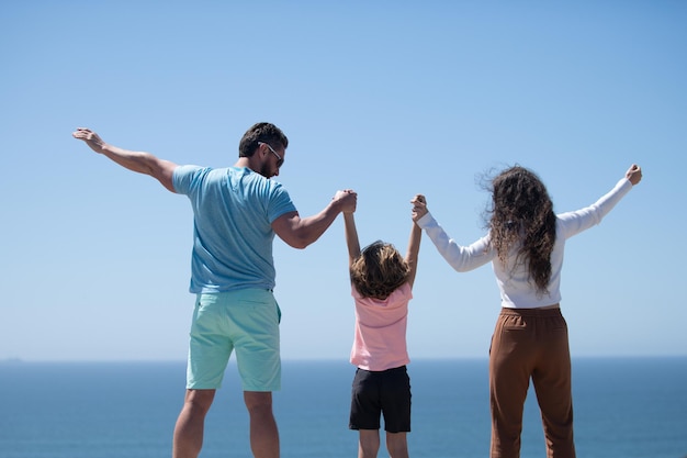 Vista traseira de uma jovem família feliz caminhando na praia, criança com pais de mãos dadas.