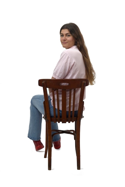 Vista traseira de uma jovem sentada na cadeira virada e olhando para a câmera no fundo branco