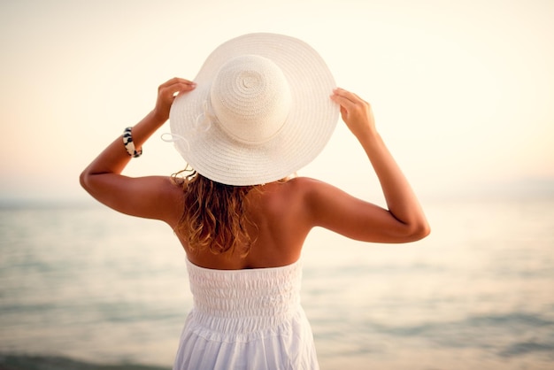 Vista traseira de uma linda mulher de vestido branco e chapéu branco de verão.