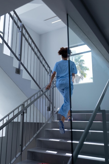 Vista traseira de uma médica mestiça usando jaleco subindo escadas no hospital