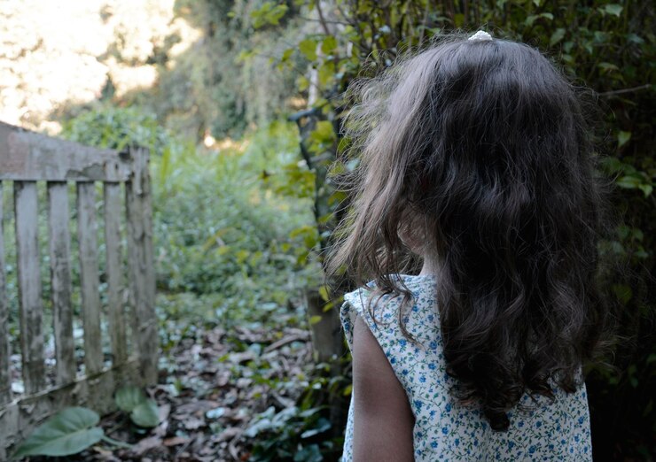Foto vista traseira de uma menina de pé junto a árvores no quintal