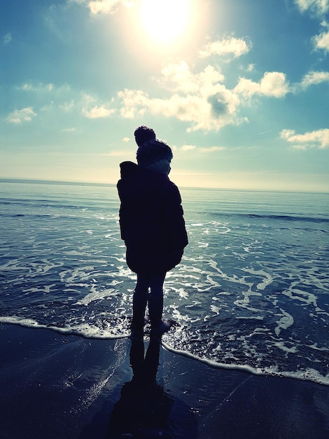 Vista traseira de uma menina de pé na costa na praia