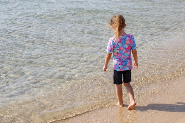 Vista traseira de uma menina em um maiô colorido na praia do mar