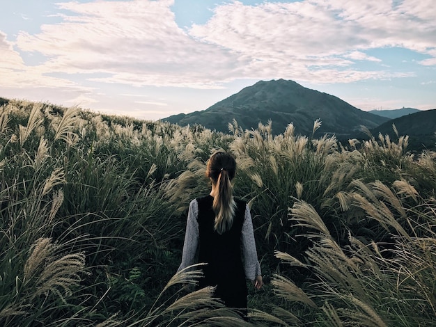 Vista traseira de uma menina no meio de plantas no campo contra o céu