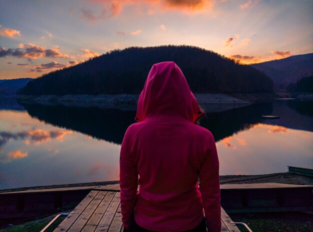 Foto vista traseira de uma mulher adulta de pé no cais sobre o lago contra o céu durante o pôr-do-sol