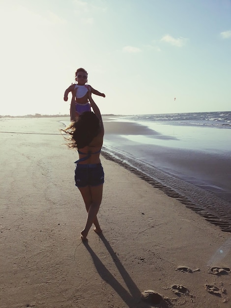 Vista traseira de uma mulher brincando com sua filha enquanto está de pé na praia