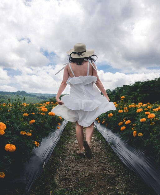 Vista traseira de uma mulher caminhando em meio a plantas em flor contra o céu nublado