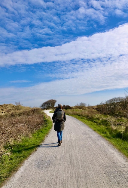 Vista traseira de uma mulher caminhando na estrada sob um céu azul e nublado