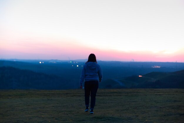 Foto vista traseira de uma mulher caminhando na paisagem contra o céu durante o pôr do sol