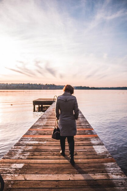 Foto vista traseira de uma mulher caminhando no cais sobre o lago contra o céu