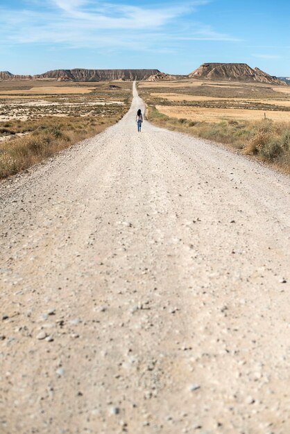 Foto vista traseira de uma mulher caminhando por uma estrada de terra no deserto contra o céu