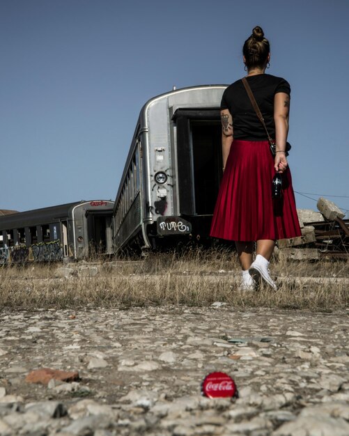 Foto vista traseira de uma mulher caminhando por vagões de trem abandonados no campo