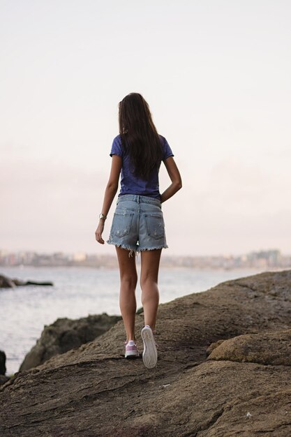 Foto vista traseira de uma mulher caminhando sobre uma rocha na praia contra o céu