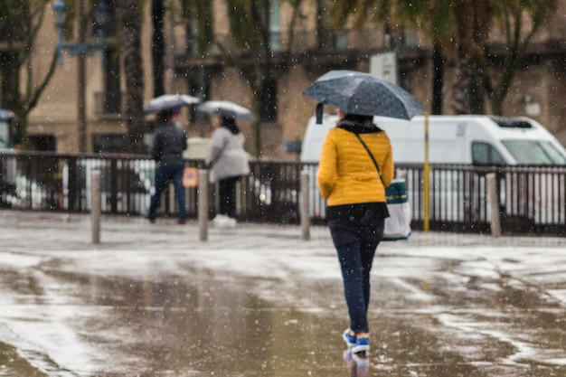 Vista traseira de uma mulher com guarda-chuva caminhando na rua molhada da cidade durante a monção