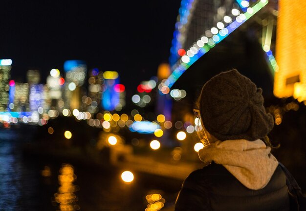 Vista traseira de uma mulher contra a cidade iluminada à noite