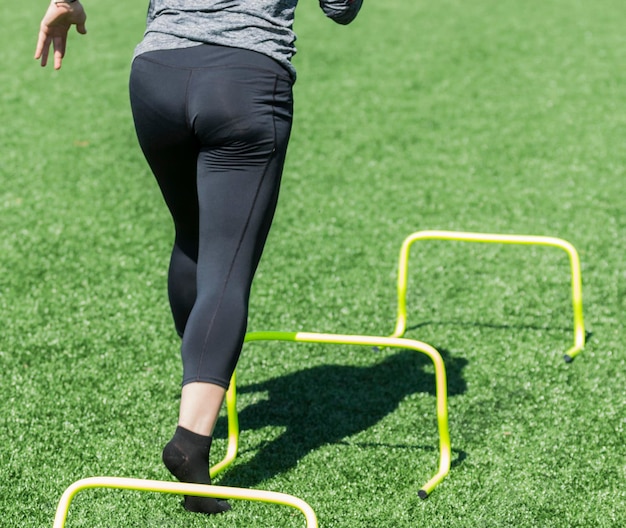 Vista traseira de uma mulher correndo sobre obstáculos em grama