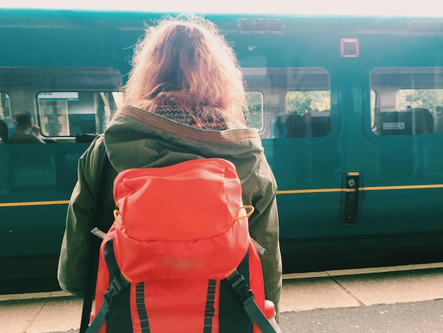 Vista traseira de uma mulher de mochila de pé na frente do trem na estação