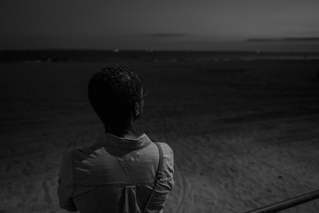 Foto vista traseira de uma mulher de pé contra a praia à noite