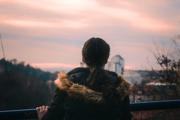 Vista traseira de uma mulher de pé contra o céu durante o pôr do sol