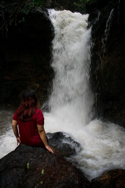 Foto vista traseira de uma mulher de pé contra uma cachoeira