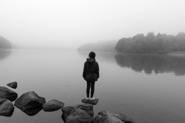 Vista traseira de uma mulher de pé em uma rocha ao lado de um lago