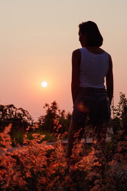 Foto vista traseira de uma mulher de pé junto a plantas contra o céu durante o pôr do sol