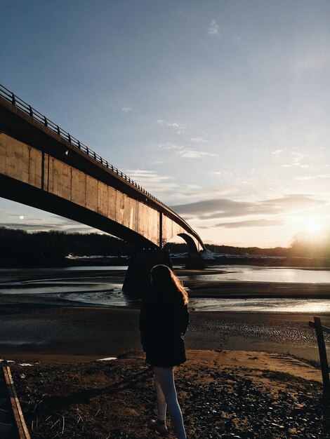 Foto vista traseira de uma mulher de pé na costa pela ponte contra o céu