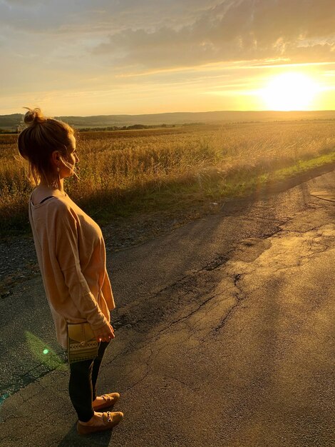 Foto vista traseira de uma mulher de pé na estrada contra o céu durante o pôr do sol