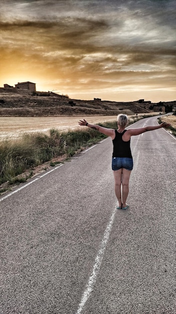 Foto vista traseira de uma mulher de pé na estrada contra o céu durante o pôr do sol