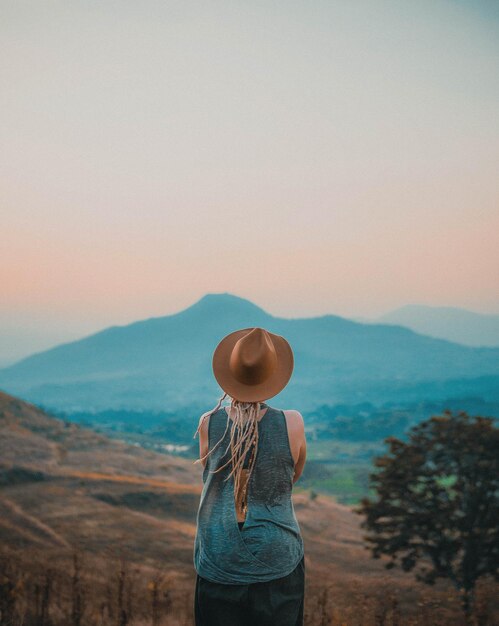 Vista traseira de uma mulher de pé na montanha contra o céu durante o pôr do sol