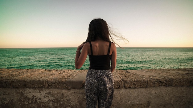 Foto vista traseira de uma mulher de pé na praia contra o céu claro