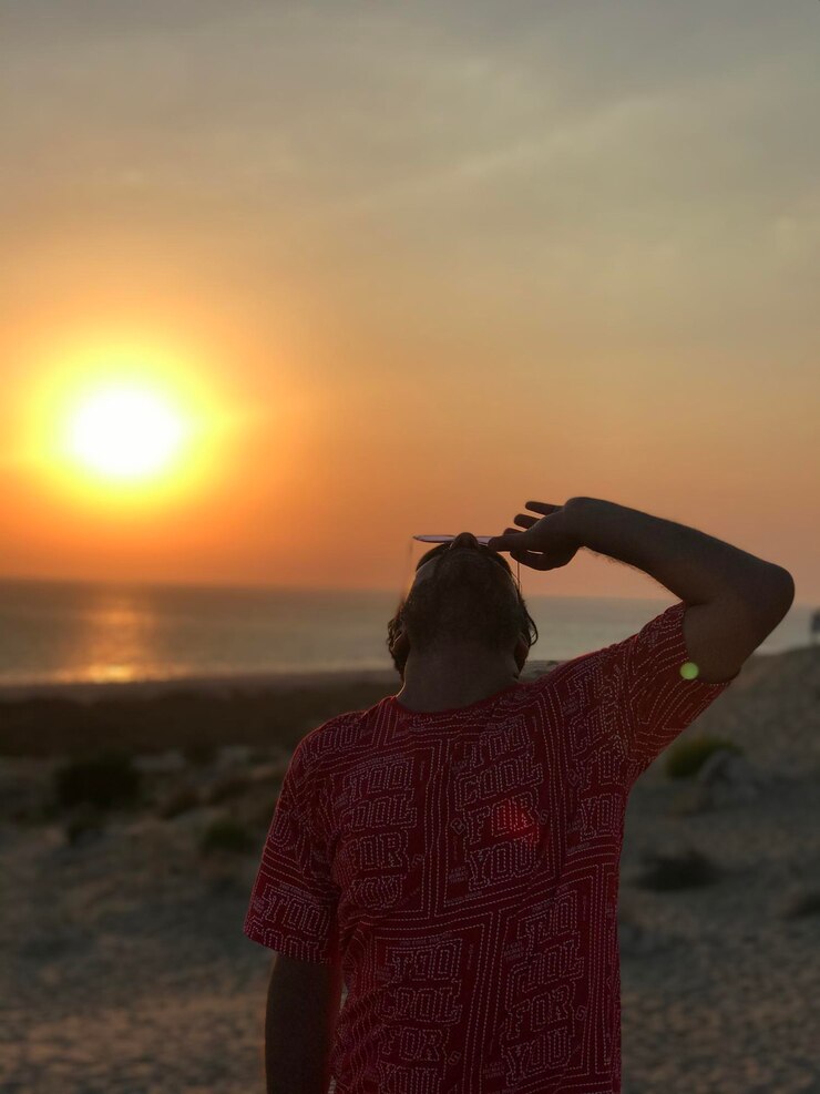 Foto vista traseira de uma mulher de pé na praia durante o pôr-do-sol