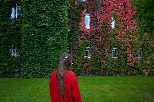 Foto vista traseira de uma mulher de pé no campo contra um edifício coberto de hera