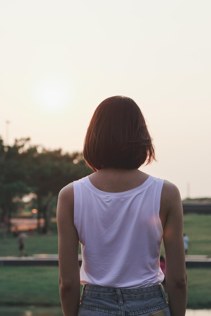 Foto vista traseira de uma mulher de pé no parque durante o pôr do sol