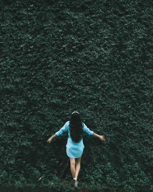 Foto vista traseira de uma mulher despreocupada com os braços estendidos de pé contra as plantas