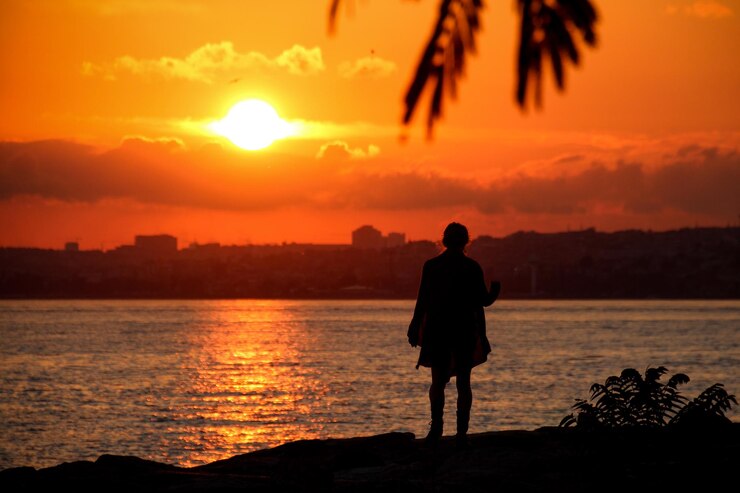 Foto vista traseira de uma mulher em silhueta de pé contra o mar durante o pôr-do-sol