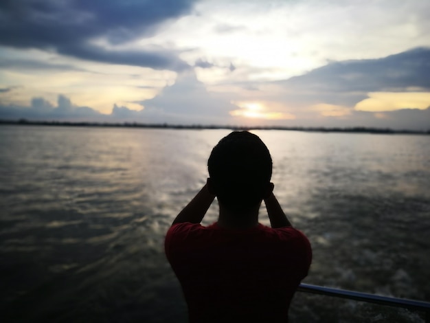 Foto vista traseira de uma mulher em silhueta de pé contra o mar durante o pôr-do-sol