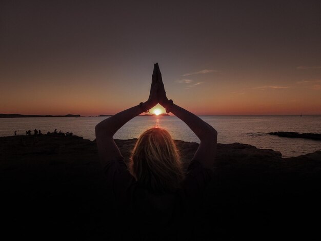 Foto vista traseira de uma mulher em silhueta na praia durante o pôr-do-sol