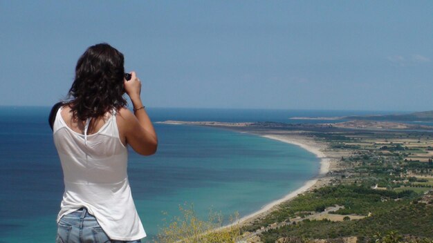 Foto vista traseira de uma mulher fotografando a costa contra o céu