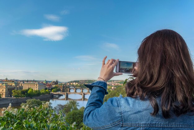 Vista traseira de uma mulher fotografando na cidade contra o céu azul