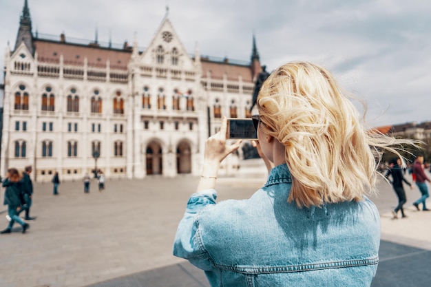 Vista traseira de uma mulher fotografando um edifício na cidade