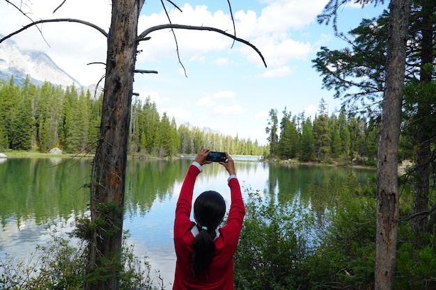 Vista traseira de uma mulher fotografando um lago usando um smartphone na floresta