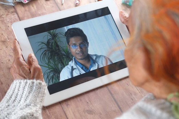 Vista traseira de uma mulher idosa em consulta online com um médico em um tablet digital