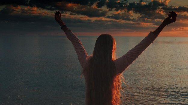 Foto vista traseira de uma mulher na praia contra o céu durante o pôr-do-sol